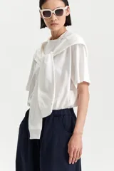 Camiseta blanca de manga corta con un buzo blanco de manga larga cosido en la parte superior, creando un efecto de prenda superpuesta atada al cuello.