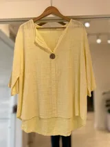Blusa amarilla de mangas tres cuartos, escote en V y un botón grande de madera al frente.