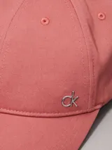 Gorra de béisbol color rosado, confeccionada en sarga de algodón orgánico, con cierre ajustable y herraje metálico con el monograma 'ck' en la parte frontal.