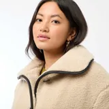 Campera de efecto borreguito en color beige, con cuello amplio y cierre frontal de botones negros. Presenta ribetes negros en contraste en el cuello, la apertura frontal y los puños. Marca Kiabi.