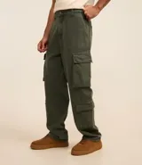 Pantalón baggy color verde militar, confeccionado en sarga de algodón, con cintura con trabillas, cierre con botón y cremallera, y bolsillos cargo laterales. Modelo holgado de estilo vintage.