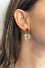 Caravanas colgantes con diseño de corazón de cristal transparente facetado y piedra superior ovalada color naranja rojizo, montadas en base dorada.