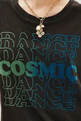 Remera de algodón color negro con efecto lavado, de corte clásico y manga corta. Presenta un estampado frontal con la palabra 'COSMIC' en el centro rodeada por la palabra 'DANCE' repetida en tonos degradados de verde a azul.