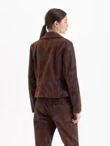 Chaqueta de corte recto con cierre frontal, cuello camisero amplio y bolsillos delanteros con solapa y botones metálicos. Presenta un diseño estampado con líneas verticales en tonos marrón y azul.
