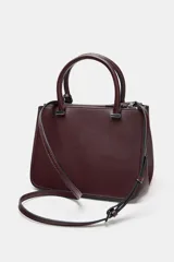 Bolso tipo mini city de diseño estructurado, con doble asa de mano y asa bandolera extraíble. Cuenta con doble compartimento exterior con cierre de cremallera metálica y un compartimento central con cierre imantado. Incluye un detalle de etiqueta colgante decorativa.