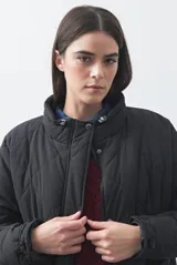 Campera acolchada de nylon color negro, con cuello alto, cierre frontal y botones a presión. Presenta un diseño de rombos y forro interior suave.