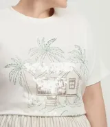 Remera de algodón color blanco, manga corta y cuello redondo, con un estampado lineal de una cabaña tropical rodeada de palmeras y la frase "Summer feeling". Algunas partes del estampado tienen lentejuelas transparentes.