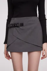 Minifalda gris de corte cruzado con detalle de cinturón lateral en cuero sintético negro con hebilla metálica.