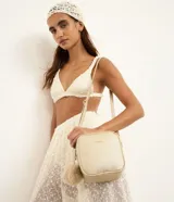 Cartera bandolera estructurada Satinato de color dorado, con textura granulada, cierre doble, correa transversal ajustable y un pompón colgante.