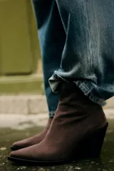 Botín de mujer color marrón oscuro, de serraje con acabado en punta y cierre mediante cremallera. Tiene un tacón estilo cowboy.