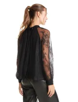 Blusa de encaje negro con cuello halter y mangas largas transparentes. Presenta un diseño elegante con detalles florales en el encaje y cierre con lazo en la espalda.