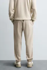 Pantalón tipo jogger de corte slim fit, confeccionado en tejido de algodón con elasticidad. Presenta cintura elástica ajustable con cordón, bolsillos frontales, bolsillos traseros de vivo y bajos con puños elásticos.