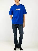 Remera de algodón azul con cuello redondo y corte relajado, que presenta un estampado gráfico con el logo de la marca en el pecho.