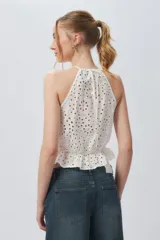 Top blanco sin mangas con cuello halter, bordado con calados y elástico con volado en la cintura.