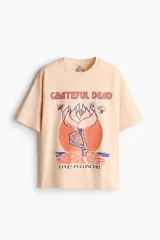 Remera oversized de punto de algodón color salmón, con hombros caídos, cuello redondo ribeteado y diseño estampado en el frente con la temática de Grateful Dead.