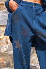 Pantalón azul con estampado de estrellas brillantes, de corte recto y fluido, cintura alta con trabillas para cinturón, cierre con botón y cremallera, bolsillos laterales.