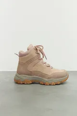 Zapatilla tipo hiking de caña media, confeccionada en una combinación de símil cuero y nylon en tonos beige y rosa suave. Presenta cordones al tono, interior acolchado para mayor abrigo y suela de goma dentada en color marrón con entresuela gris.