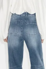 Jean de tiro alto en denim de algodón con leve stretch. Presenta piernas amplias, corte holgado, bolsillos tipo parche en la parte frontal y raya marcada a lo largo de las piernas. Incluye cierre y botón metálico.