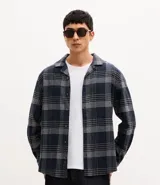 Camisa de manga larga confeccionada en franela de algodón, con cuello bowling y cierre frontal de botones. Presenta un diseño de estampado a cuadros en tonos azul marino y gris, con un corte regular.