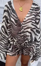 Vestido corto con estampado animal print tipo zebra, escote en V cruzado, mangas largas amplias y detalle de volados en la parte inferior.