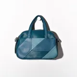 Bandolera de cuero sintético color turquesa con diseño geométrico en tonos de azul. Tiene doble asa corta y correa larga regulable.