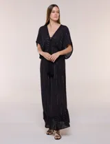 Vestido largo negro confeccionado en gasa con hilos de lurex en relieve vertical. Presenta escote en V profundo con lazo frontal y borlas, mangas holgadas tipo kimono, cintura elastizada y falda fluida con ruedo con volante.