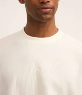 Remera marrón de poliéster y elastano con textura de pana, cuello redondo, manga corta y bordado centralizado de lettering minimalista.