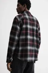 Camisa de franela de manga larga con cuello inglés, tapeta lisa, canesú en la espalda, bolsillo superior abierto y bajo redondeado. Presenta un patrón de cuadros en tonos negro, gris y granate.