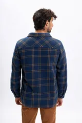 Sobrecamisa de polar a cuadros en tonos azul marino y marrón, con interior forrado en corderito, cierre frontal de botones, cuello clásico y bolsillos frontales en el pecho.