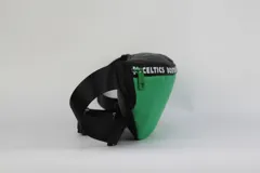 Riñonera de nylon color verde con detalles en negro. Presenta una cinta superior con la inscripción 'Boston Celtics' repetida y el logo del equipo estampado en la parte inferior derecha. Cuenta con cierre frontal y correa regulable.