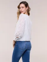 Blusa blanca de organza con textura devoré floral, silueta semiholgada y forro interno. Tiene escote bote, mangas largas abullonadas con transparencias, puños anchos con botones y ruedo elastizado.