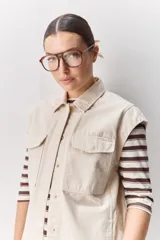 Chaleco de algodón color beige, de calce relajado, con cuello clásico, hombros amplios, cierre frontal con broches metálicos y bolsillos delanteros con solapa.