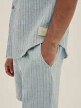 Conjunto de camisa de manga corta con cuello solapa y short con cordón ajustable, ambos en tejido ligero a rayas verticales celestes y blancas.