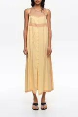 Vestido midi de línea A color amarillo, confeccionado en mezcla de lyocell y viscosa, con botones frontales, escote cuadrado y tirantes finos. Presenta detalles de encaje en contraste y mini tablas verticales en el frente.