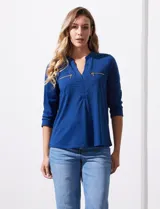 Blusa azul con cuello a la base y escote en V. Tiene bolsillos con cierre metálico.