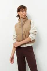 Chaleco puffer color beige, sin mangas, con cuello alto y cierre frontal con cremallera.