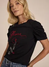 Remera negra de tejido de punto con estampado frontal de la palabra 'Glamour' y dos labiales. Tiene escote redondo, hombros fruncidos abullonados y mangas cortas.