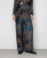 Pantalón ancho de tiro alto con efecto plisado (crinkle) y estampado abstracto en tonos marrón topo y azul. Presenta un diseño cruzado en el frente con cierre de botón y cintura elástica.