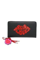 Billetera rectangular negra con cierre perimetral, decorada con un aplique en forma de labios rojos que contiene la inscripción 'Oreiro Love'. Incluye un colgante lateral con cordón rojo y un dije en forma de flor rosa con la misma inscripción.