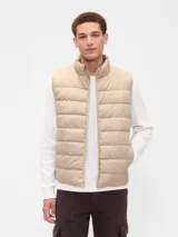 Chaleco puffer acolchado de color beige, con cierre frontal de cremallera, cuello alto y logo de la marca bordado en el pecho.