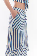 Falda midi confeccionada en algodón y lino con diseño de rayas verticales en tonos amarillo, azul y rojo. Presenta recortes diagonales y un lazo lateral para atar en la cintura, con detalle de volados en el ruedo.