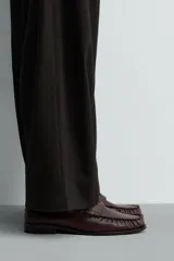 Mocasín de vestir tipo penny loafer en color bordó con acabado desgastado, diseño de antifaz en el empeine y suela de goma a contraste con pequeño tacón.