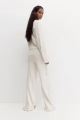 Pantalón de punto suave color beige, de tiro alto con cintura elástica, perneras rectas, secciones laterales con diseño pointelle y detalle de volados en el bajo.