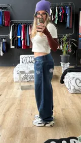 Pantalón de jean azul oscuro de corte wide leg, con diseño holgado y tiro medio. Presenta un pequeño bordado con alas en el bolsillo delantero.