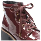 Bota acordonada de estilo urbano en acabado charol color bordó. Presenta una suela de goma robusta con plataforma y un taco cuadrado de altura media. Incluye ojales metálicos dorados y cordones al tono.