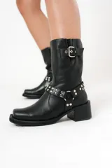 Bota biker de caña media color negro, con hebilla en la parte superior y detalle de aro y tachas en la parte inferior.