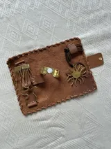 Set de accesorios compuesto por un collar, un brazalete y dos pares de aros, todos elaborados en bronce, presentados en un sobre de cuero marrón tipo gamuza.