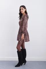 Vestido corto con estampado de cebra en tonos marrón y negro. Presenta mangas largas con puños elásticos, volados en los hombros y cintura elástica con lazo ajustable. Tiene tachas metálicas termo adhesivas en el escote y hombros.