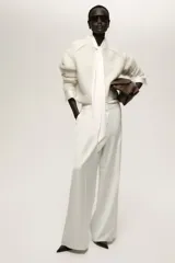 Pantalón de vestir blanco con cintura clásica, cierre con botón oculto y corchete. Presenta bolsillos al bies, bolsillo trasero decorativo y piernas amplias con pliegues marcados adelante y atrás.