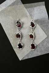 Par de aros colgantes de plata 950 con piedras naturales granate facetadas en formas de gota, ovalada y redonda, unidas por eslabones con engarces de contorno irregular.